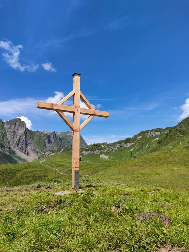 neues Holz-Gipfelkreuz auf Alpkuppe, Felsberge, blauer Himmel