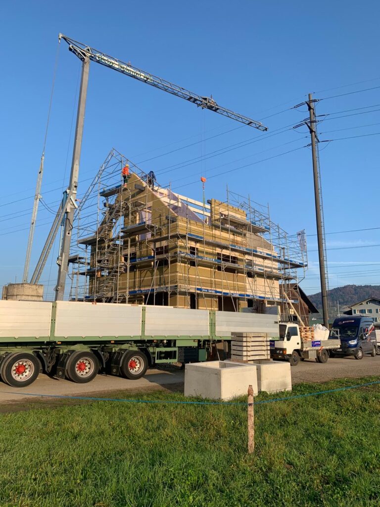 Chrumbitzi-Wohnhaus im Holzbau mit Gerüst, Baukran, Lastwagen mit Elementen