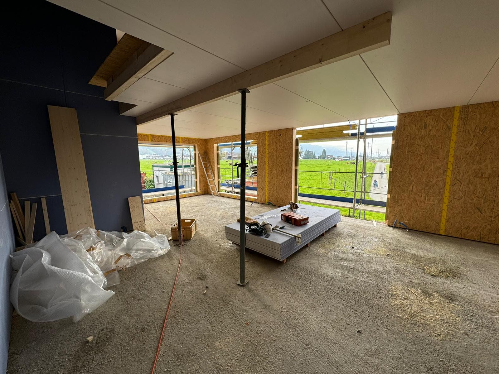 Holzbau-Innenraum mit Stützen und Blick ins Grüne, Baustellenmaterial
