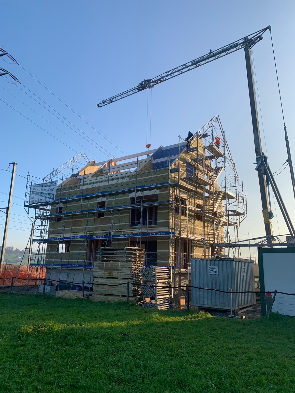 Holzbau-Rohbau mit Gerüst und Kran in Abendsonne, Wiese vorne