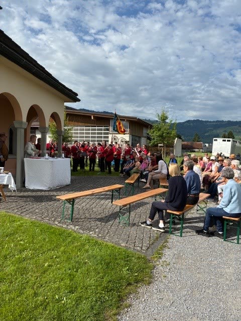 Kapelle Nuolen von der Seite, Besucher auf Bänken unter bewölktem Himmel
