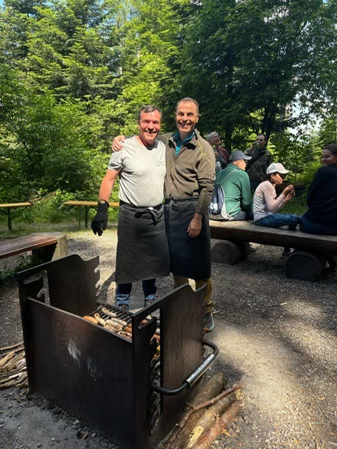 Zwei Männer mit Schürzen am Grill der Feuerstelle (Verpflegung)