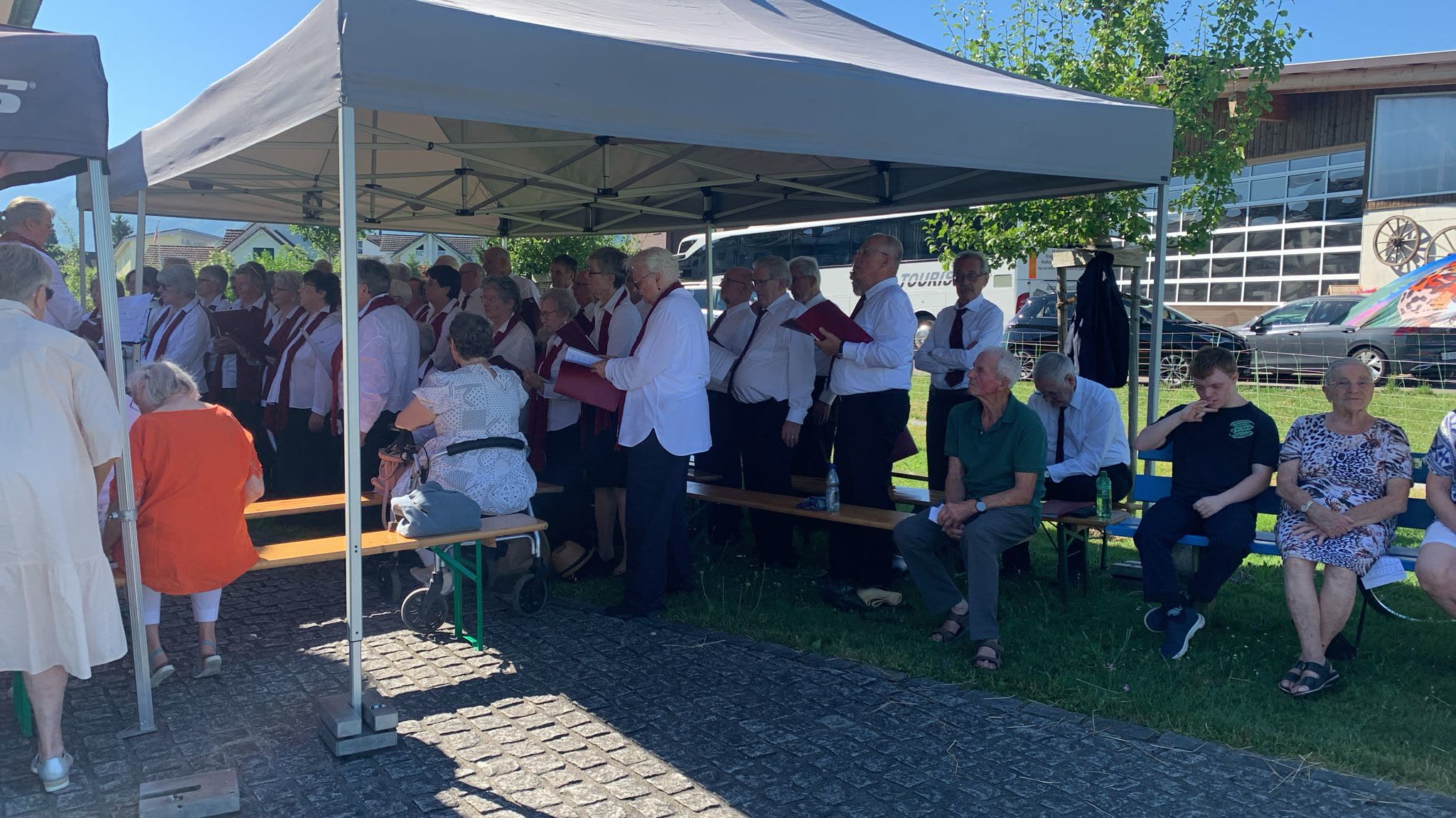 Chor und Besucher stehend unter Pavillonzelten neben Festbänken