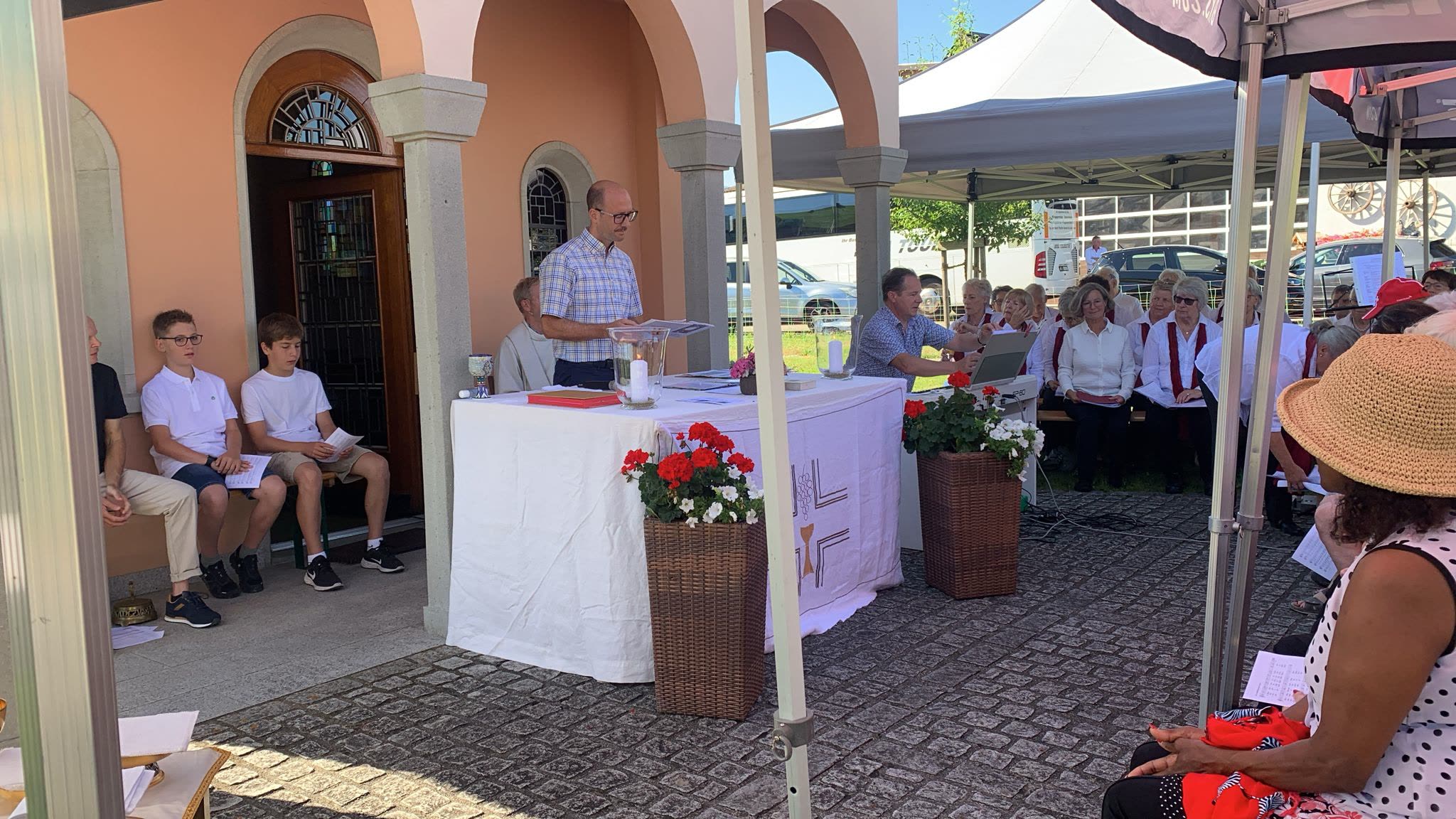 Feier vor Kapelle, Altar mit Geranien, Ministranten sitzend, Chor im Hintergrund