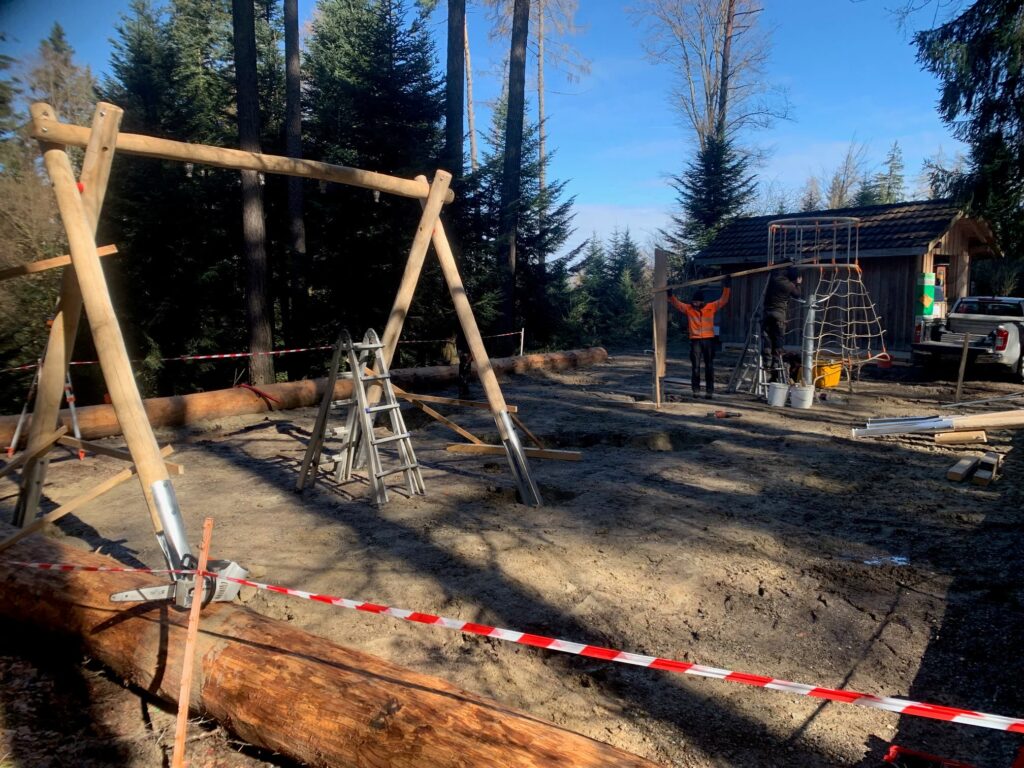 Bau des Spielplatzes bei der Feuerstelle, Schaukelgerüst aus Rundholz, Absperrband, Arbeiter