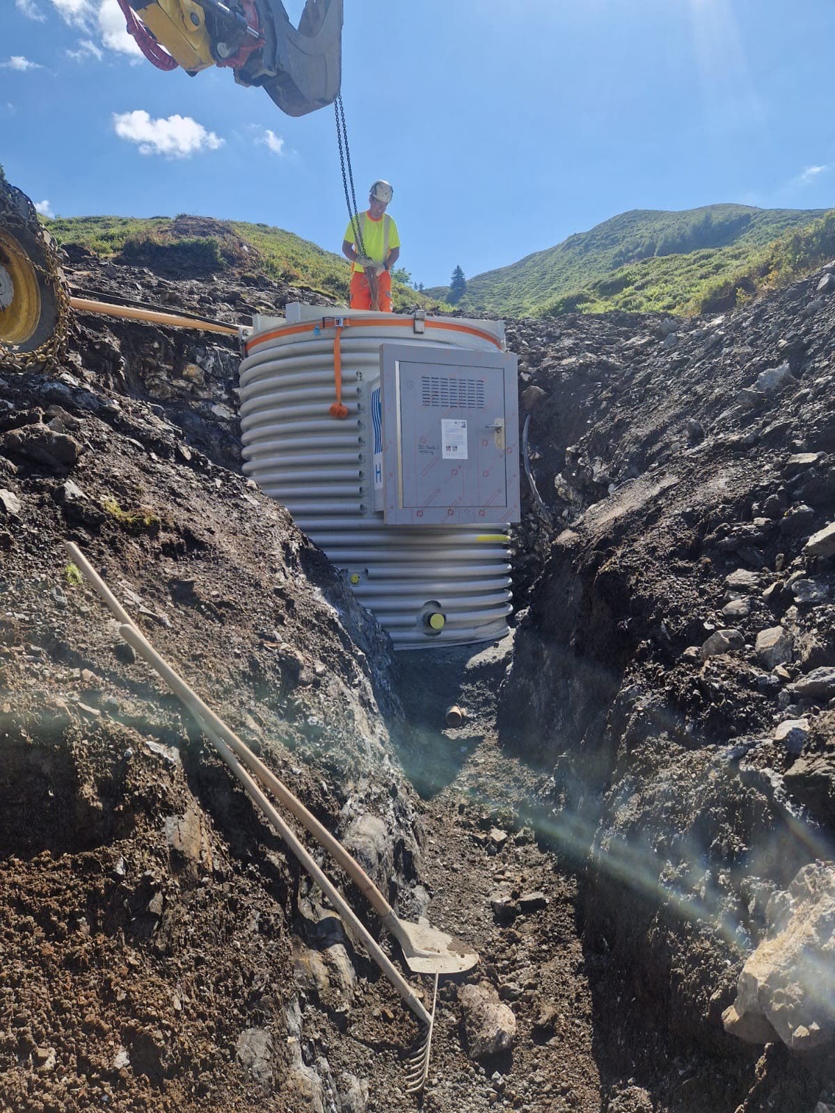 Einbau eines Wasserreservoir-Tanks in Graben, Arbeiter in Warnweste, Bagger