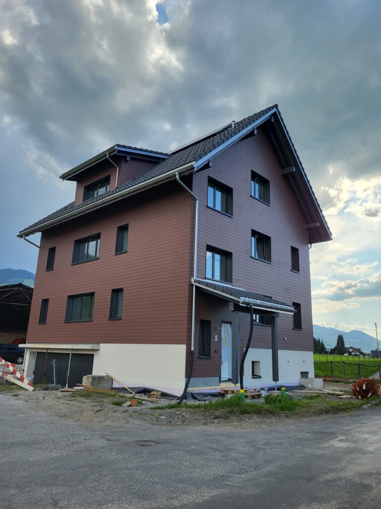 Neues Wohnhaus Chrumbitzi mit rotbrauner Fassade kurz vor der Fertigstellung, unter Wolkenhimmel