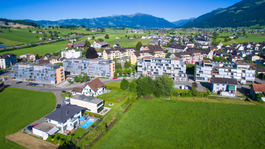 Luftbild der Überbauung Sagiareal in Wangen mit modernen Mehrfamilienhäusern, Wiesen und Bergen im Hintergrund