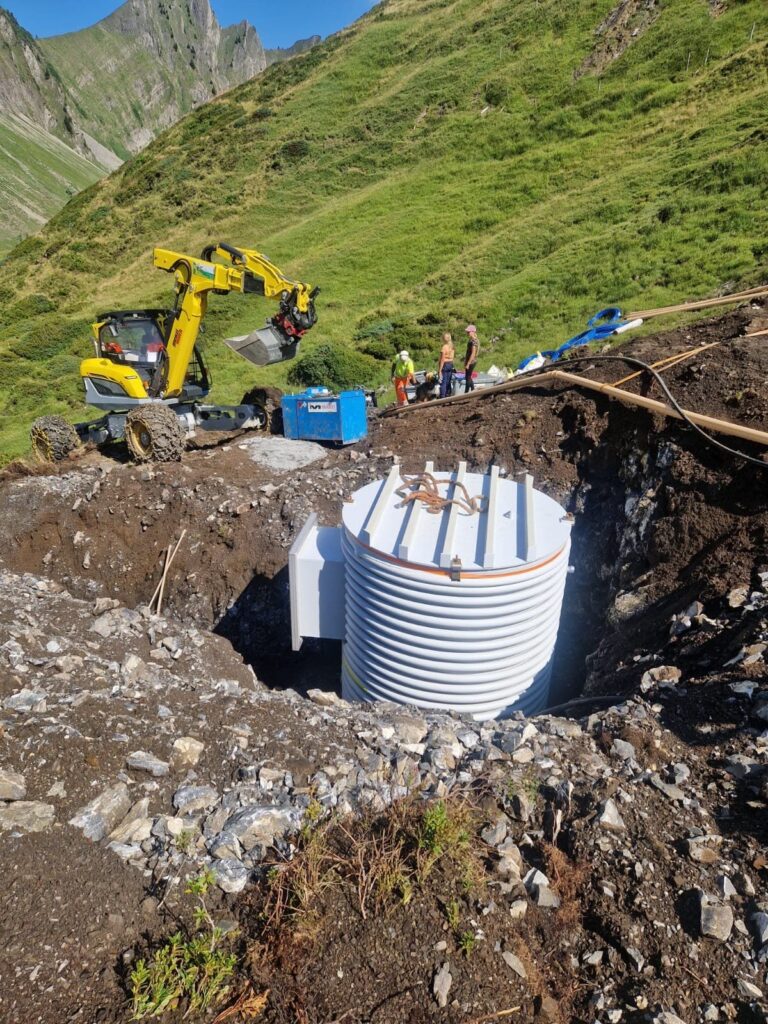 Neuer Wassertank in einer Baugrube auf der Brüschalp, dahinter ein Schreitbagger und ein steiler Alphang